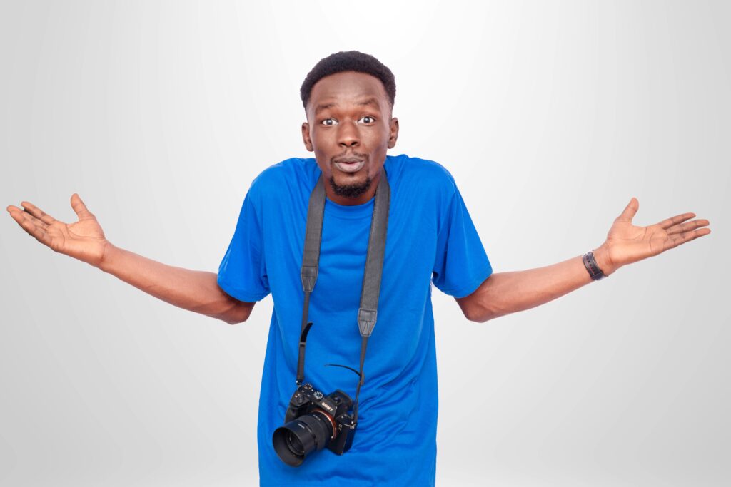 A man with a camera around his neck shrugging in confusion.